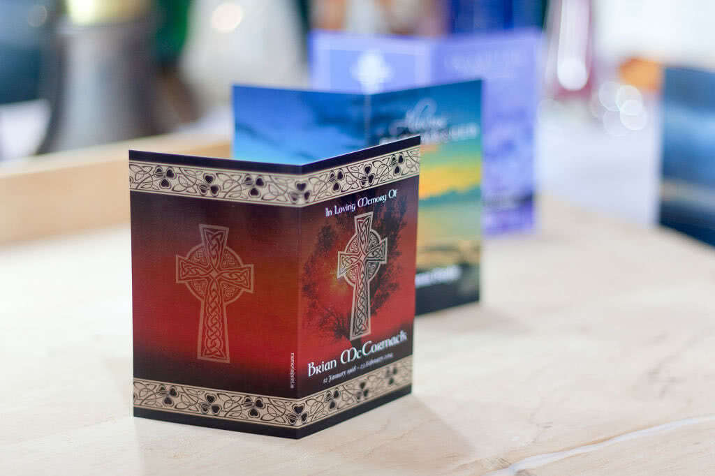 Memorial card with large Celtic cross on the front and tree in the background. Shallow DOF, more cards in the background. 