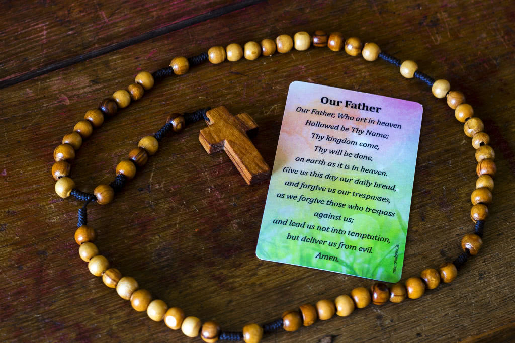 Back of a wallet memorial card with "Our Fater" prayer on it. A rosary placed around the card. 