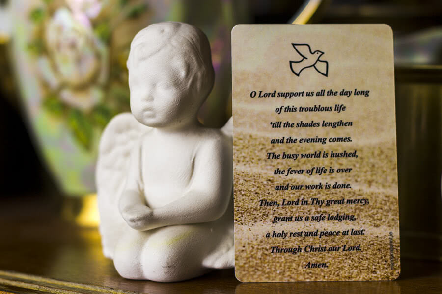 Card with O Lord support us prayer next to a small angel figure.