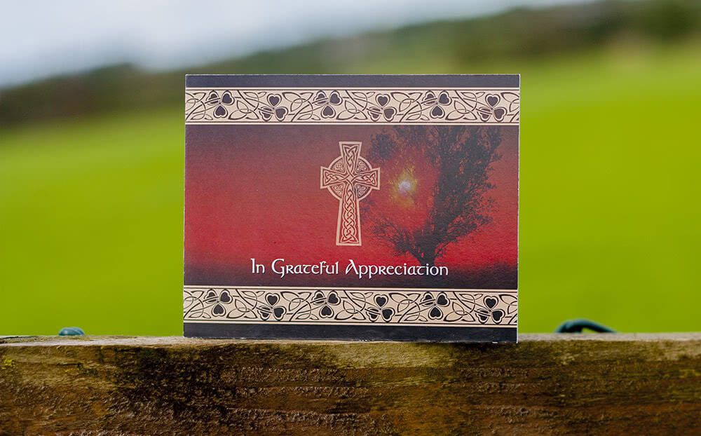 Card with Celtic cross and Irish floral pattern. Card placed on a wooden fence plank, outdoors.