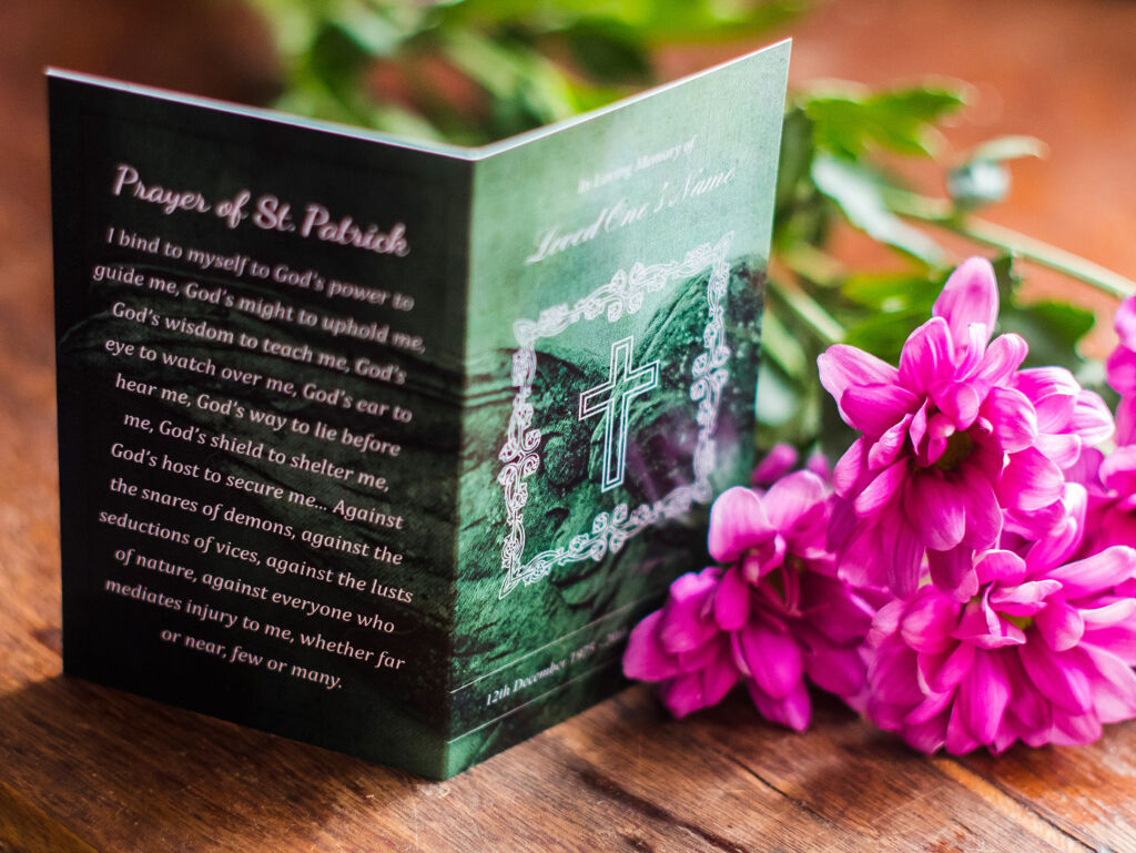 Memorial card with Prayer of St. Patrick on the back, placed next to pink flowers.